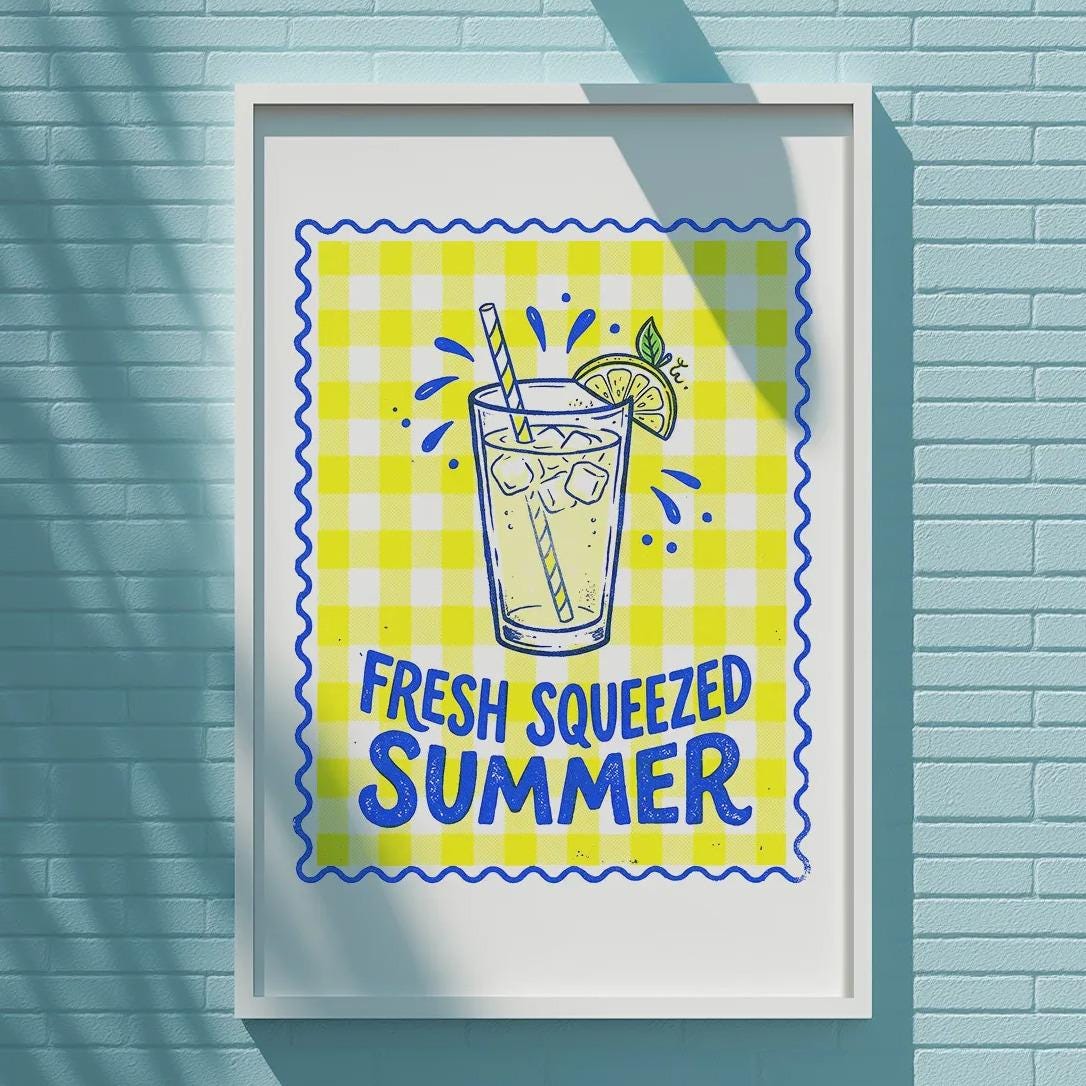 A framed poster with a yellow and blue design hangs on a blue brick wall, featuring a glass of lemonade with a lemon slice and the text "FRESH SQUEEZED SUMMER".
