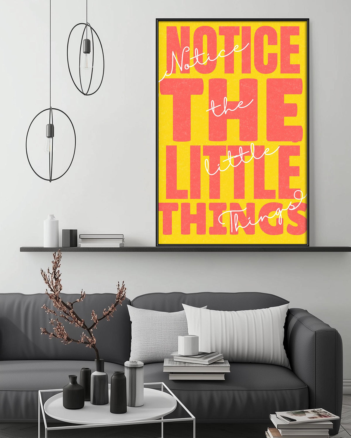 a modern living room with a gray sofa, a coffee table, and a large framed poster with the text " Notice the little things" in bold, orange and yellow letters.