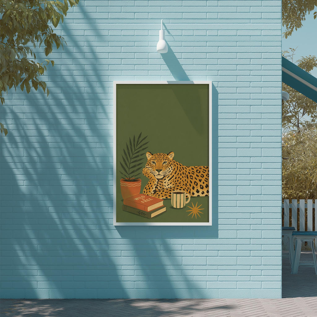 A framed illustration of a leopard is displayed on a blue wall, with a potted plant and books in the foreground.