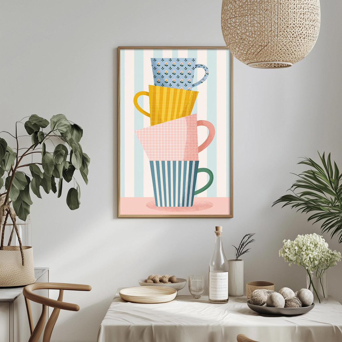 a dining table with a bowl of fruit, a bottle, and a vase of flowers, along with a framed poster of colorful mugs hanging on the wall above the table.