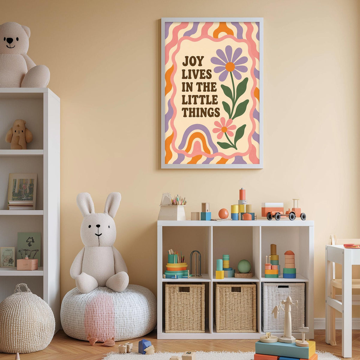 A child's bedroom with a white bookshelf, a stuffed rabbit, and a colorful poster on the wall. The poster has the text "Joy lives in the little things" and features a flower and a rainbow design.