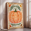 A framed illustration of an orange pumpkin with intricate floral designs surrounding it, placed on a white wall near a window.