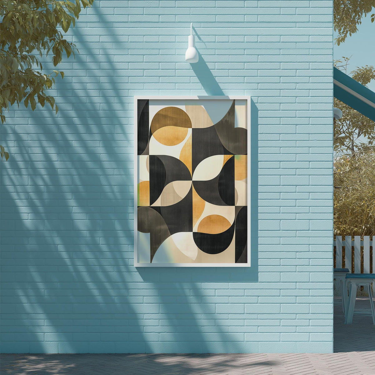 a blue wall with a framed abstract artwork hanging on it. The artwork consists of various geometric shapes and patterns in shades of black, orange, and white. The wall is situated next to a wooden deck and a tree, creating a serene and inviting outdoor setting.