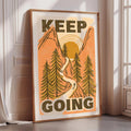 A framed poster with the text "KEEP GOING" and an illustration of a winding path through a forest with mountains in the background.
