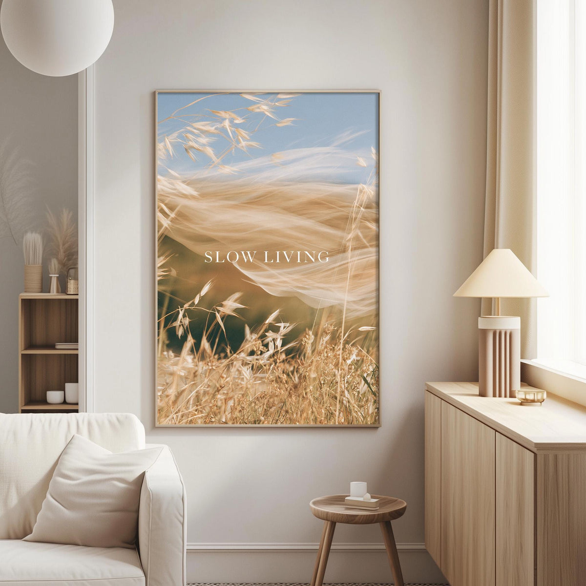 a living room with a large framed picture of a field of tall grass hanging on the wall. The picture has a serene and peaceful atmosphere, with the grass swaying gently in the breeze. The text "SLOW LIVING" is displayed on the picture, which adds a motivational and calming element to the room.