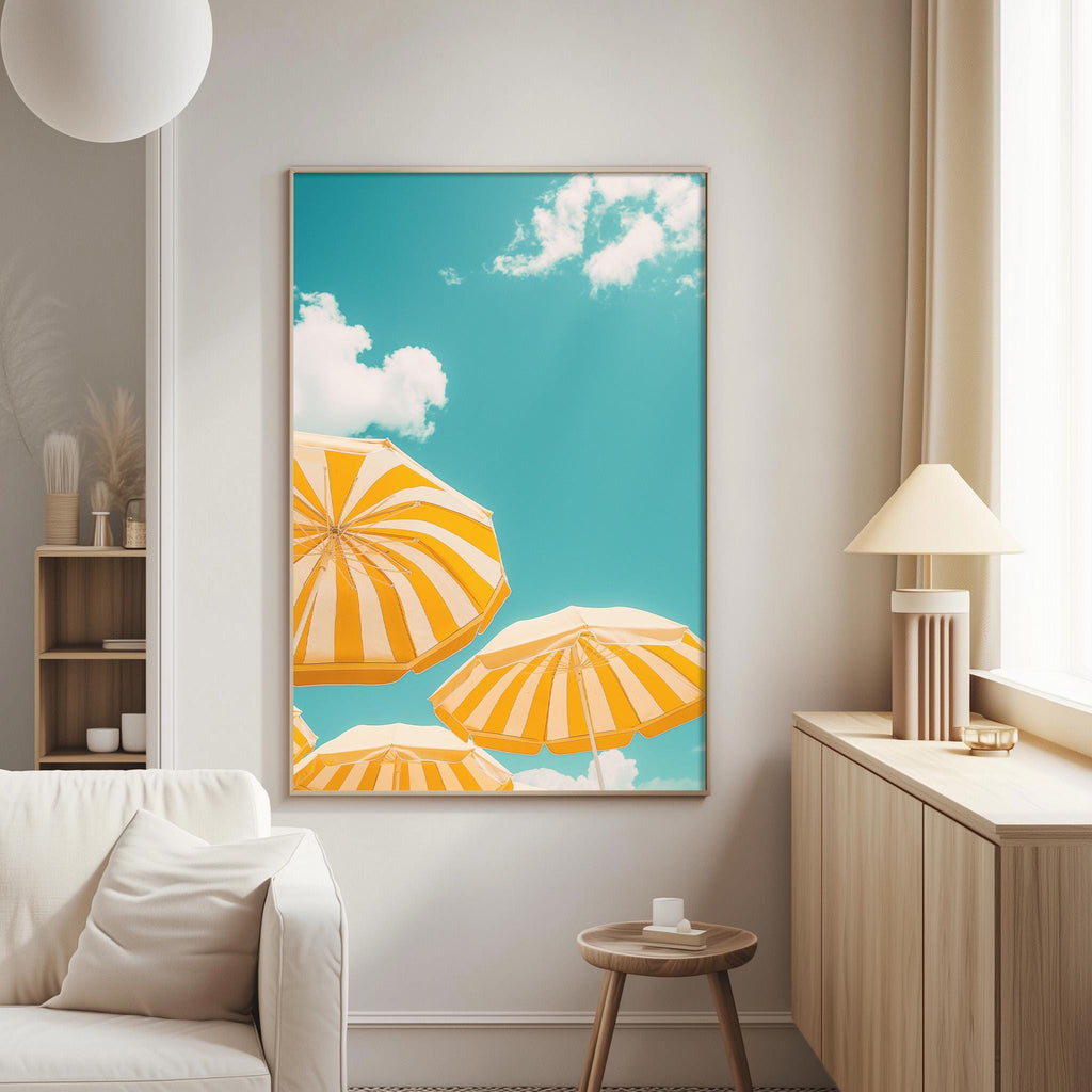 a living room with a large framed picture of three striped umbrellas against a blue sky with white clouds hanging on the wall.