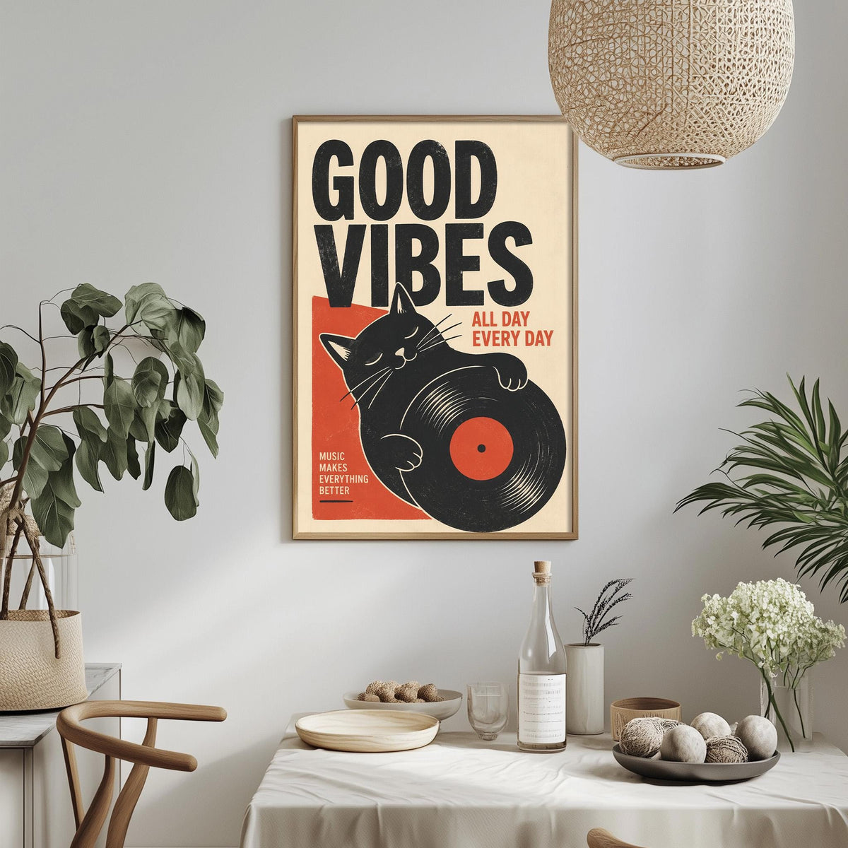 a framed poster with the text "GOOD VIBES" and an illustration of a cat holding a record album. The poster is displayed on a wall above a dining table with various items on it, such as a bottle, a bowl, and a vase.