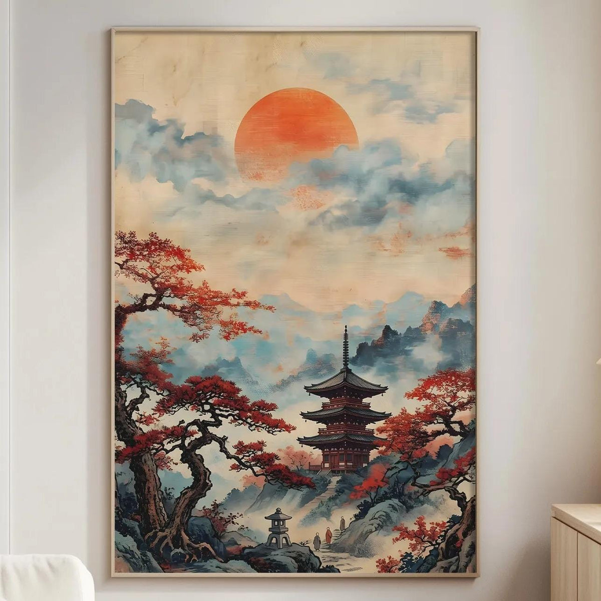 a large painting of a Japanese temple set against a mountainous landscape, with a red sun in the sky. The painting is hung on a wall in a living room, with a white sofa and a wooden side table nearby.