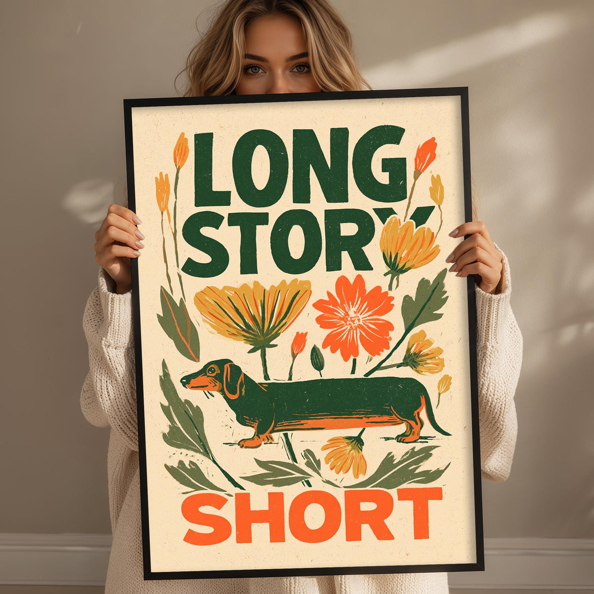 A woman holding a framed poster with the text "LONG STORY SHORT" and an illustration of a dachshund dog.