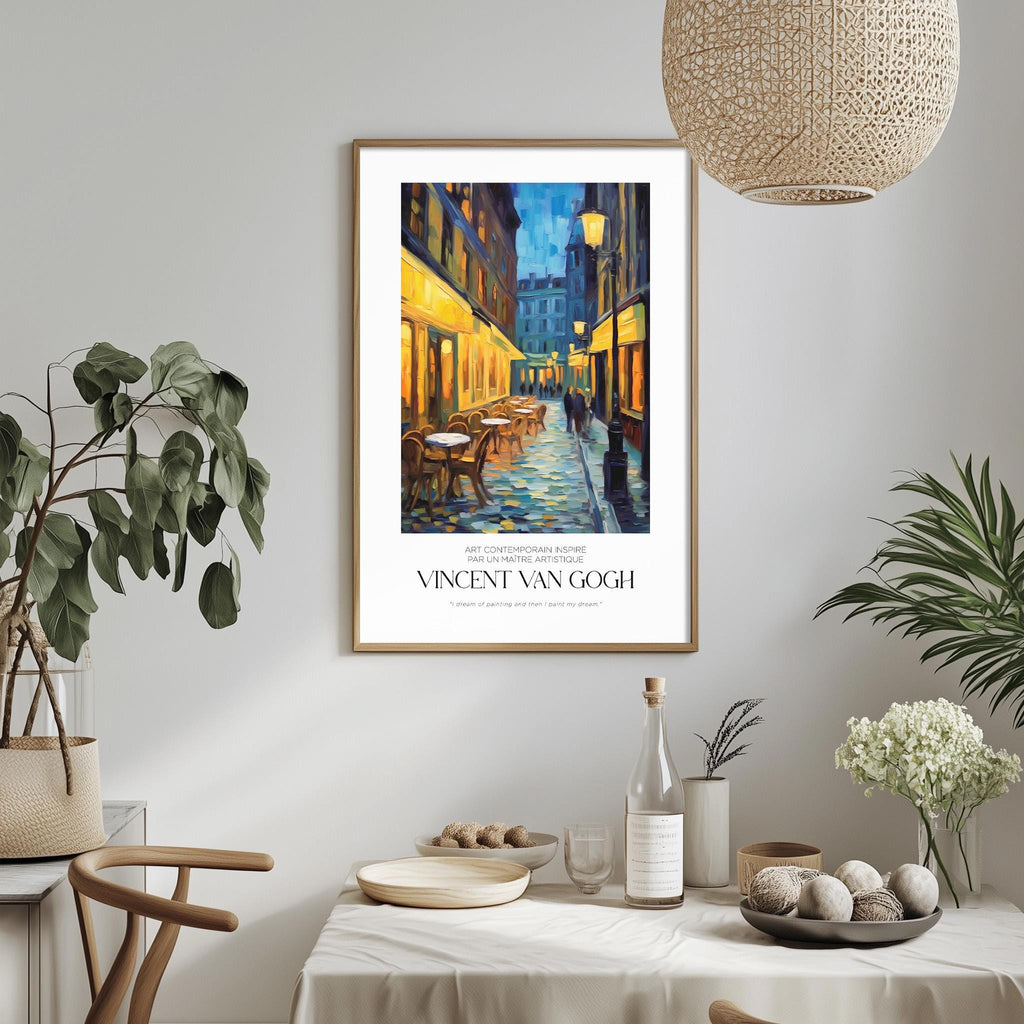 a framed painting of a street scene with a restaurant, hanging on a wall above a dining table with various decorative items and plants.