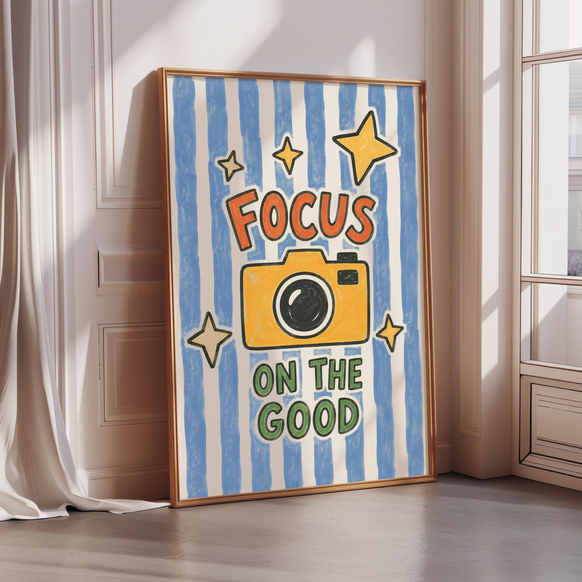 a framed poster with a camera and the text "Focus on the good" on it, placed on a wall near a window.