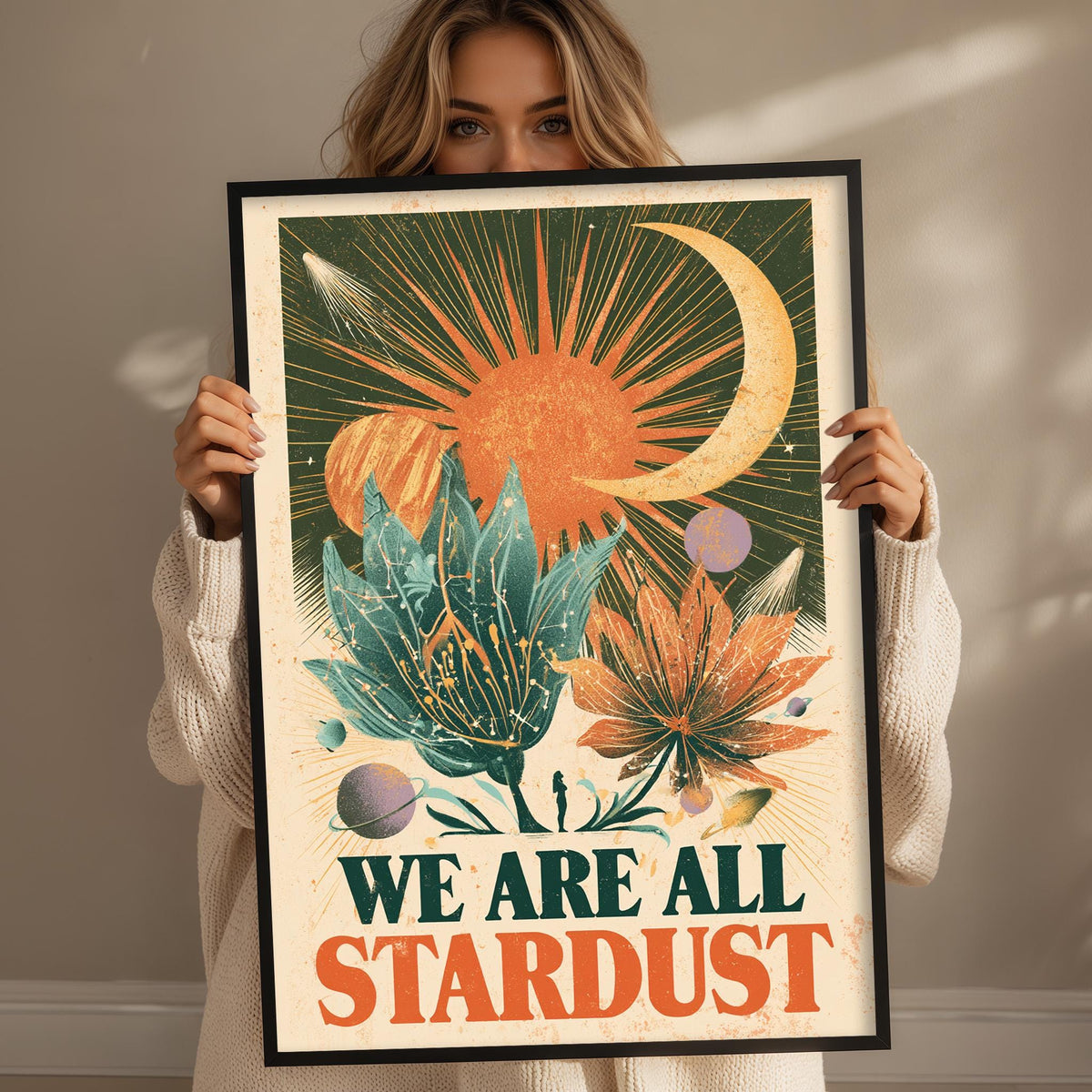 A woman is holding up a framed poster with a colorful, abstract design featuring a crescent moon, sun, and various celestial elements.