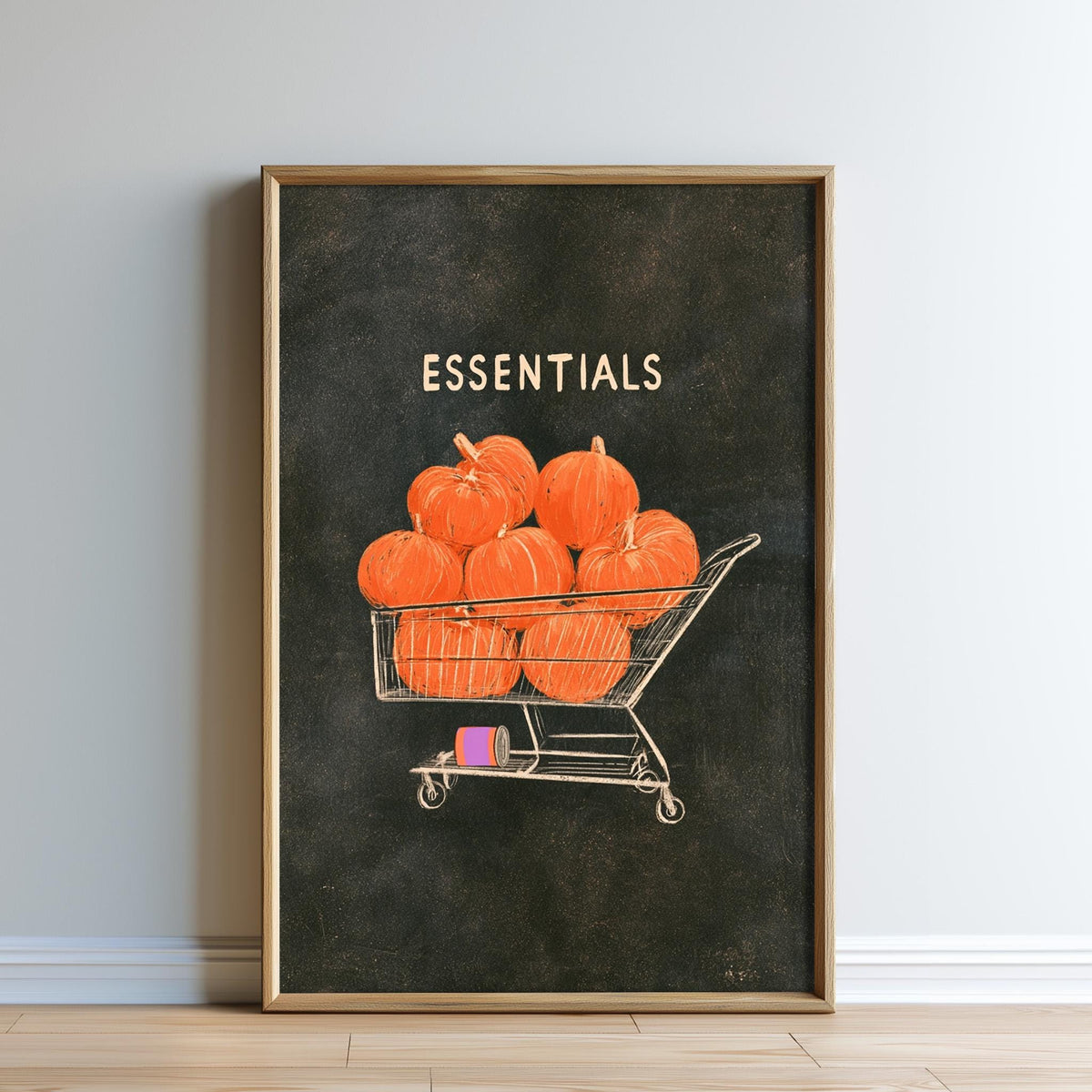 The image is a framed print depicting a shopping cart filled with orange pumpkins, with the word "ESSENTIALS" written above it.