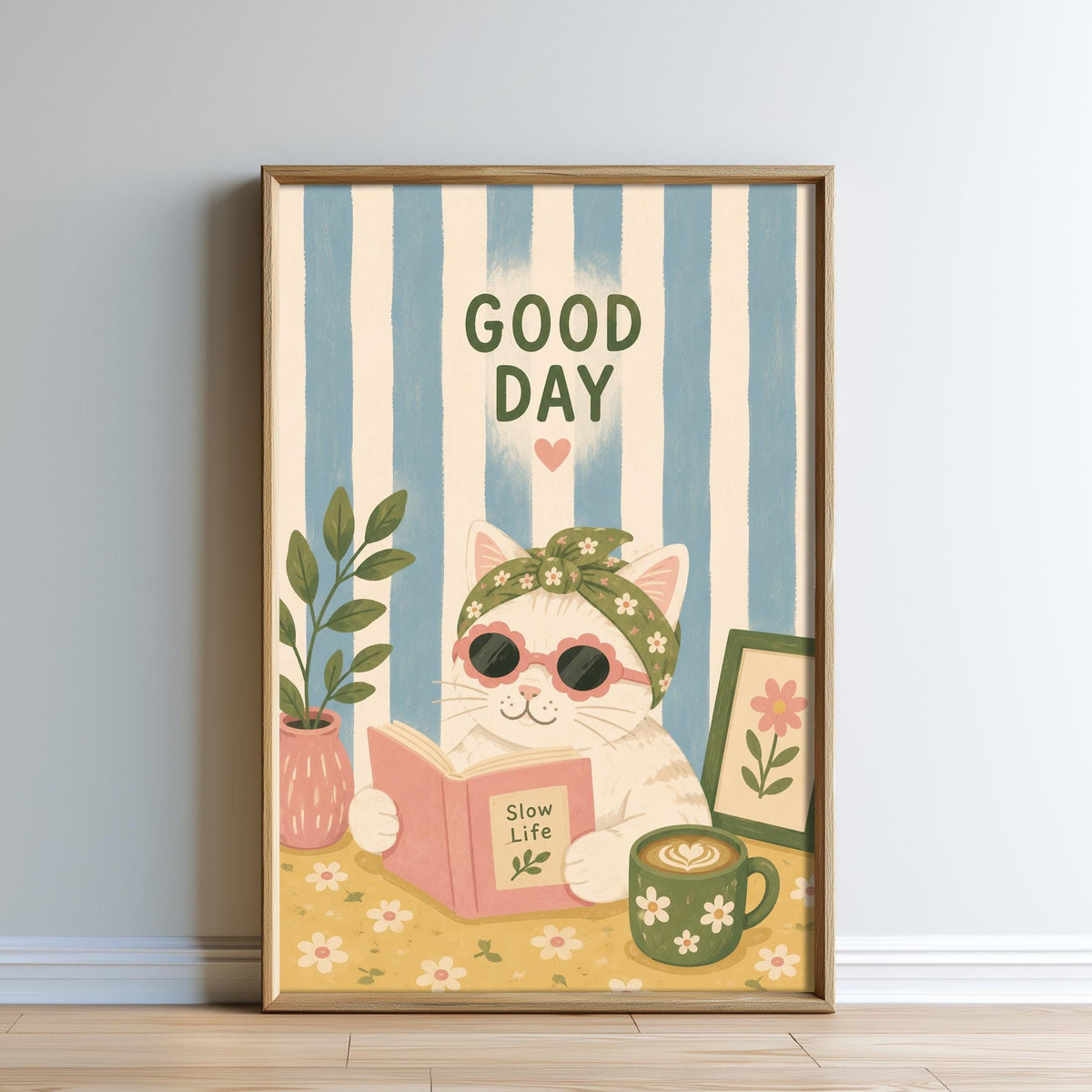 A framed illustration of a cat wearing sunglasses and a flower crown, reading a book, with a potted plant and a cup of coffee nearby, and the text "GOOD DAY" above the cat.