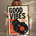 A woman holding a framed poster with a cat and the text "GOOD VIBES ALL DAY EVERY DAY"