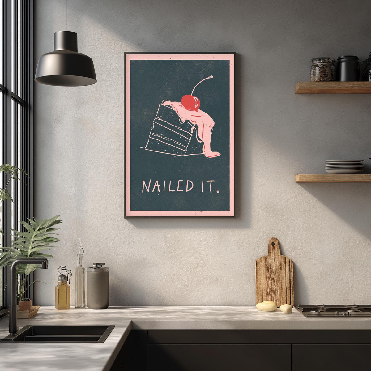 a framed poster with a whimsical illustration of a slice of cake with a cherry on top, accompanied by the text "Nailed it." The poster is displayed on a wall above a kitchen counter with various kitchen items such as a cutting board, a bottle, and a bowl.