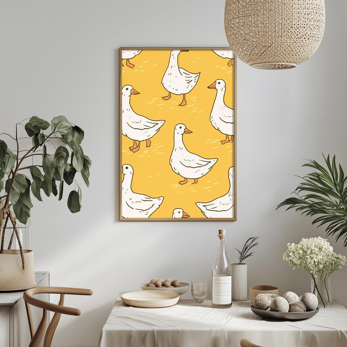 a dining table with a white tablecloth, a bowl of fruit, a bottle, and a vase with flowers. Above the table, there is a framed print of a repeating pattern of white ducks on a yellow background.