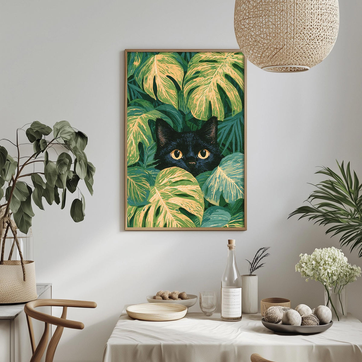 a framed painting of a black cat peeking out from behind green leaves, hanging on a wall above a dining table with various decorative items and plants.