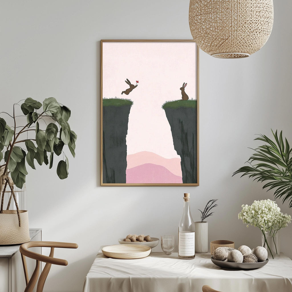 a framed artwork depicting two rabbits jumping off a cliff, with a pink and green background. The artwork is hung on a wall above a dining table with various decorative items and plants.