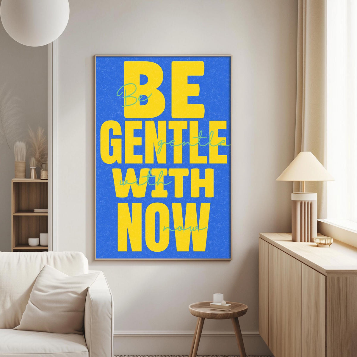 a large blue poster with the text "BE GENTLE WITH NOW" in yellow letters, hanging on a wall in a living room.