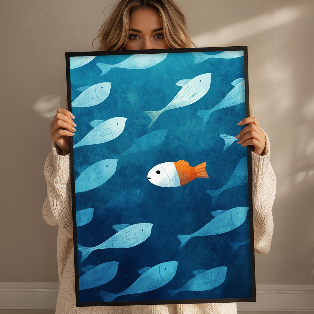 A woman holds up a framed print featuring a vibrant illustration of a fish swimming amidst a school of smaller fish in a blue ocean scene.