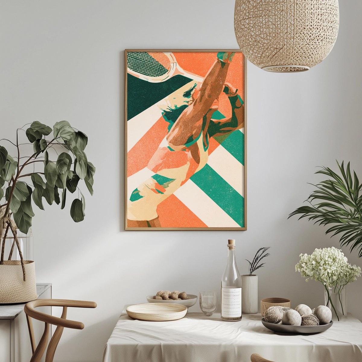 a dining table with a white tablecloth, a bowl of fruit, a bottle, and a vase with flowers. Above the table, there is a framed print of a tennis racket and ball on a striped background.