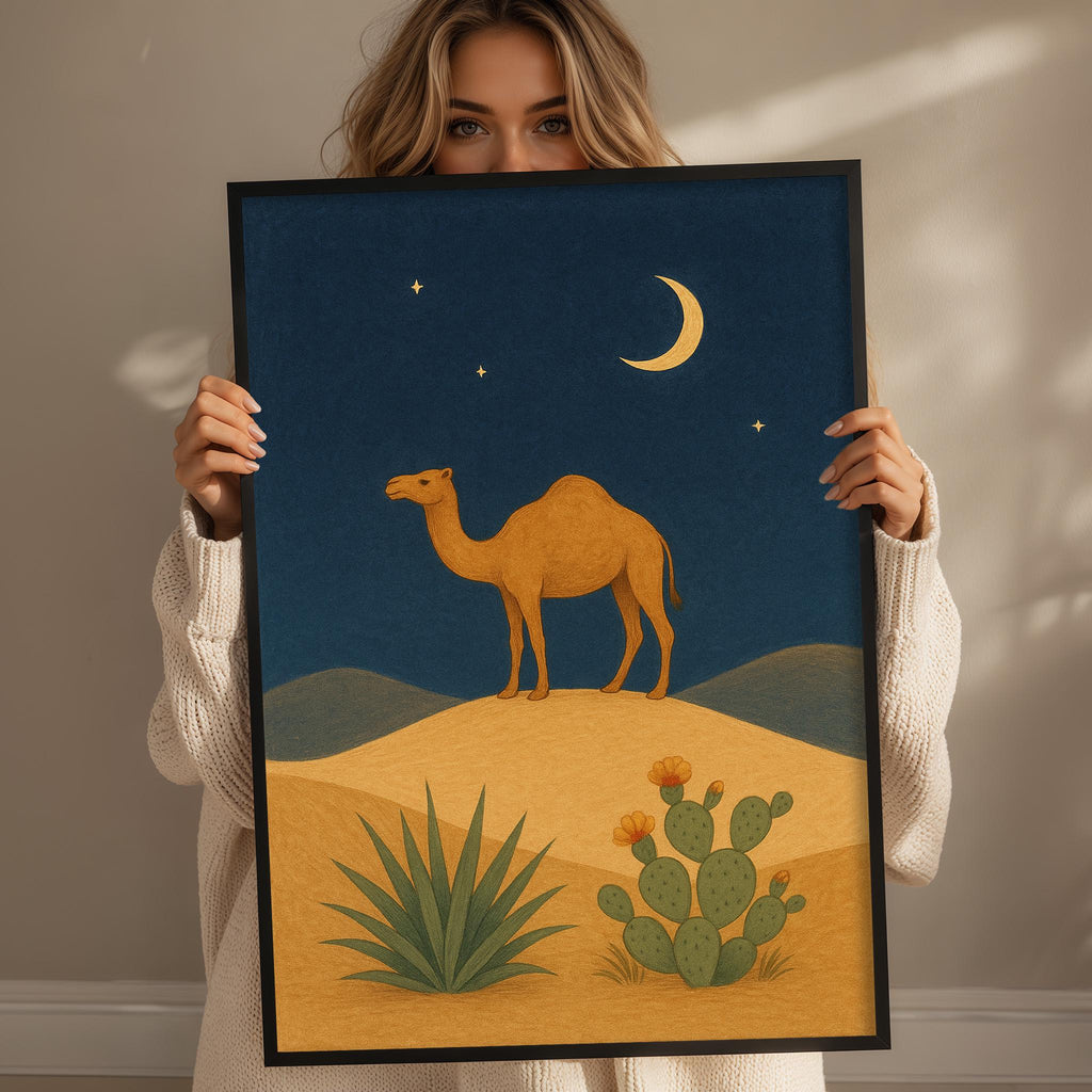 A woman holds up a framed illustration depicting a camel on a desert landscape with cacti and a crescent moon in the night sky.
