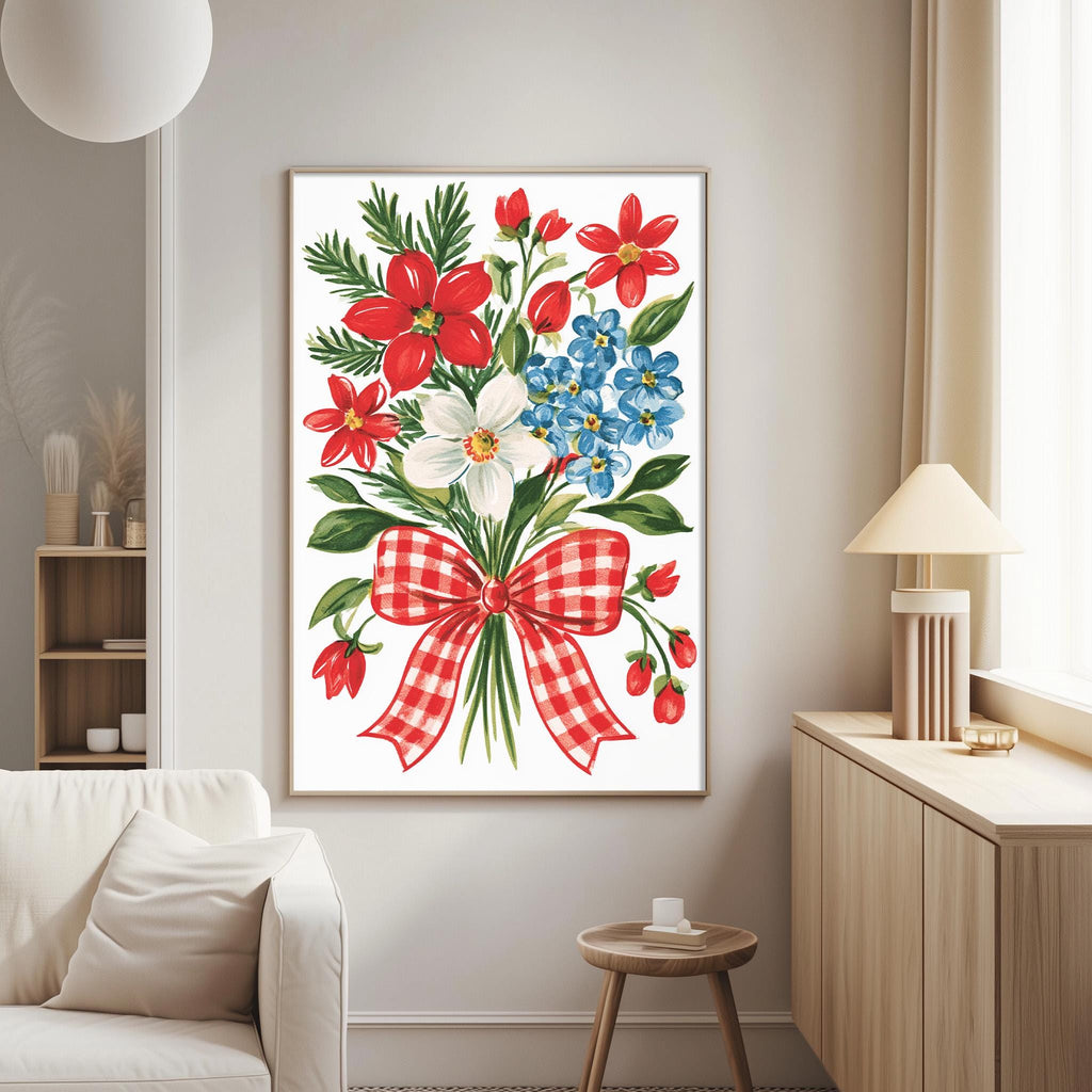 a living room with a large framed print of a floral arrangement hanging on the wall. The print depicts a bouquet of red, white, and blue flowers, along with green leaves and a red and white checkered bow. The room has a white couch, a wooden side table, and a lamp on a nearby table.