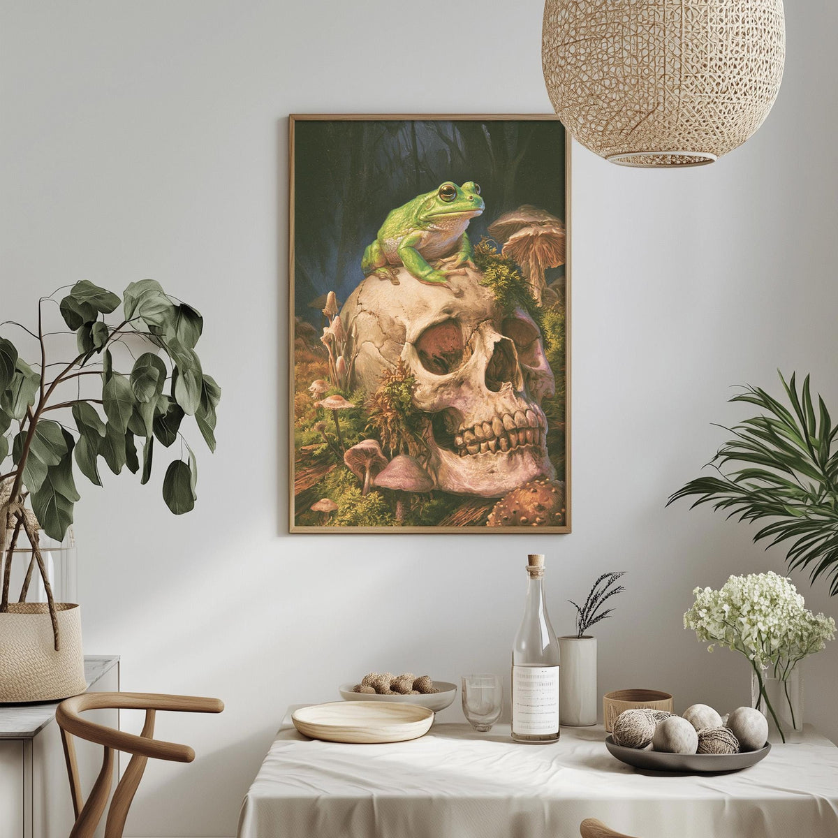 a framed painting of a frog perched on a skull, surrounded by mushrooms and plants, hanging on a wall above a table with various items on it.