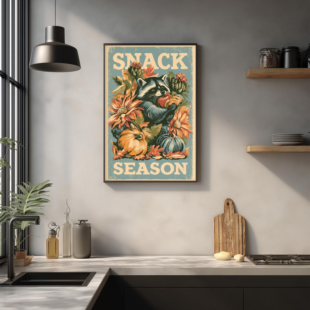 a kitchen counter with various kitchen items, including a cutting board, a knife, and a bottle. Above the counter, there is a framed poster with a raccoon and flowers, and the text "SNACK SEASON" is displayed on the poster.
