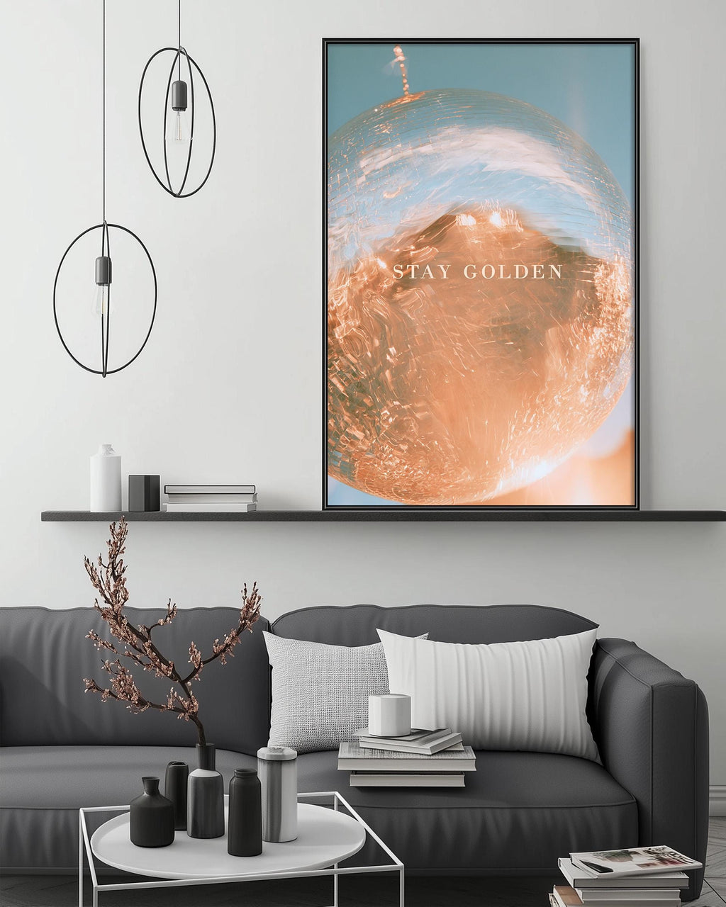 a modern living room with a gray sofa, a coffee table, and a large framed poster on the wall. The poster has a vibrant orange and blue design and the text "STAY GOLDEN" written in white.