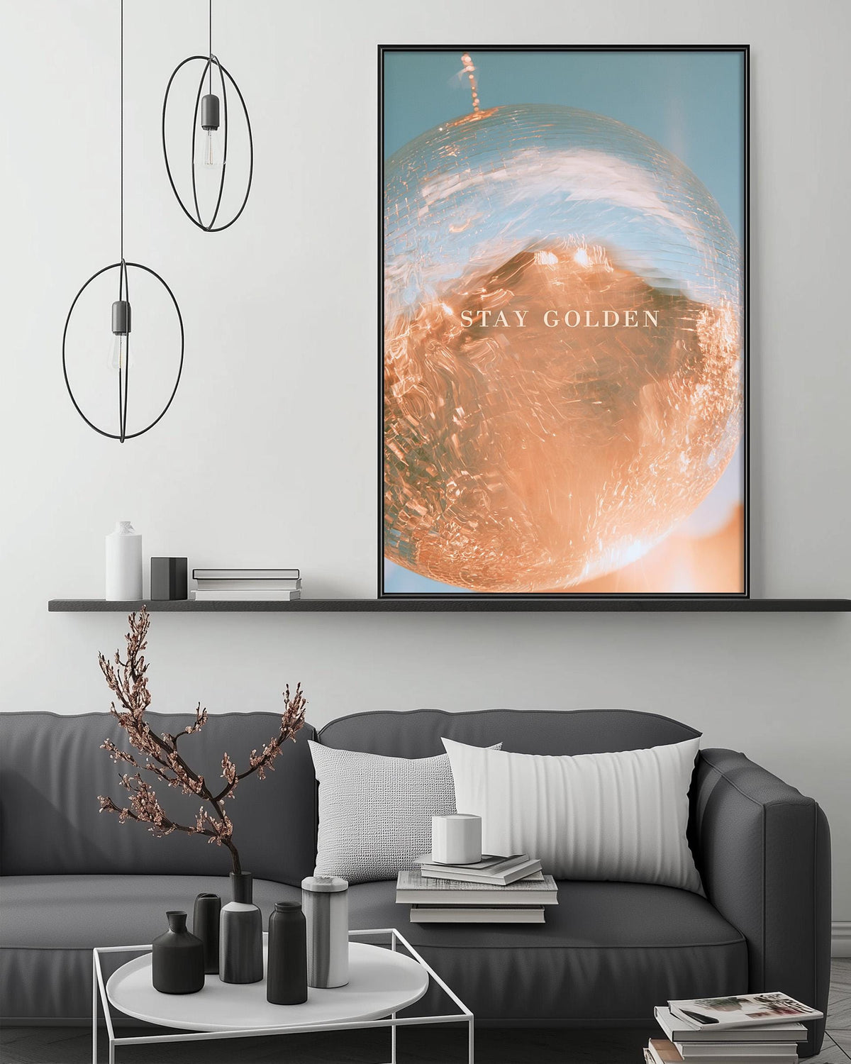 a modern living room with a gray sofa, a coffee table, and a large framed poster on the wall. The poster has a vibrant orange and blue design and the text "STAY GOLDEN" written in white.