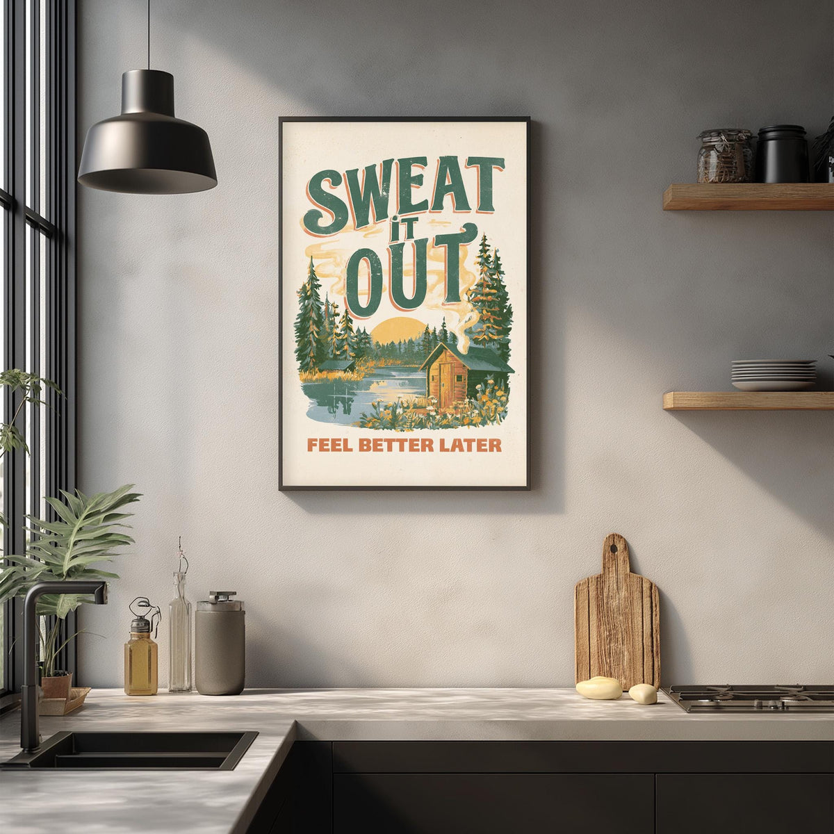 a framed poster with the text "SWEAT IT OUT" and a scenic illustration of a cabin surrounded by nature. The poster is hanging on a wall above a kitchen counter with various kitchen items such as a cutting board, a bottle, and a jar.