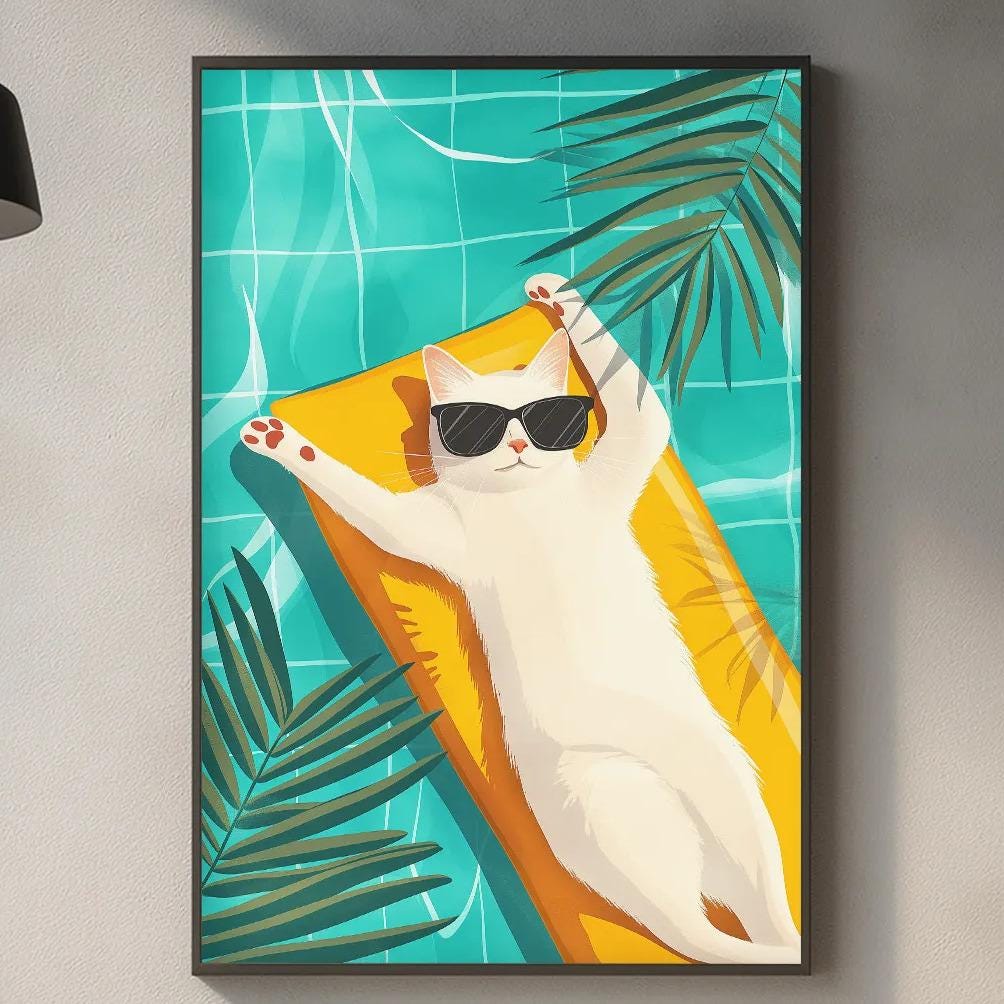 A framed illustration of a cat lounging on a beach towel, wearing sunglasses, is displayed on the wall above a kitchen counter.