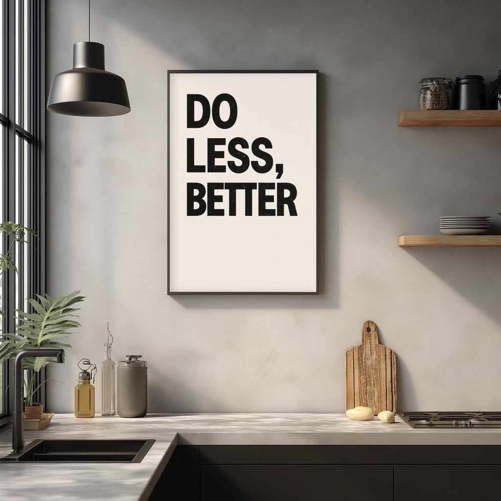a kitchen counter with a framed poster that reads "DO LESS, BETTER" hanging above it. The counter also has various kitchen items such as a cutting board, a bottle, and a bowl.