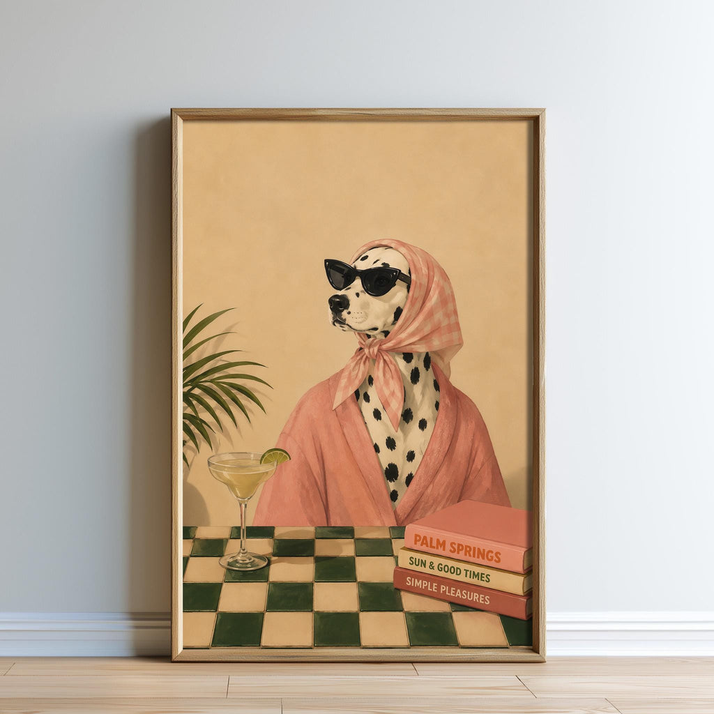 A Dalmatian dog wearing a pink robe and sunglasses is sitting at a table with a martini glass and a stack of books, with a palm tree in the background.