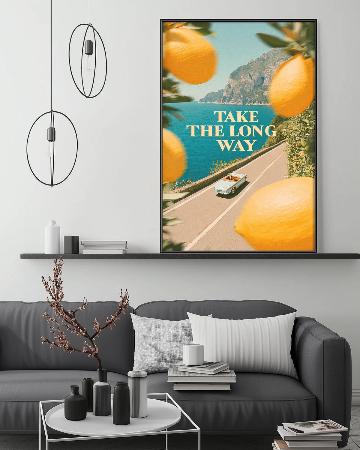 a living room with a gray couch, a coffee table, and a large framed poster hanging on the wall. The poster depicts a scenic road with a car and a scenic view of the ocean.