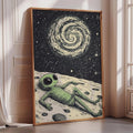 a framed illustration of an alien lying on the ground, looking up at the night sky with a spiral galaxy above.