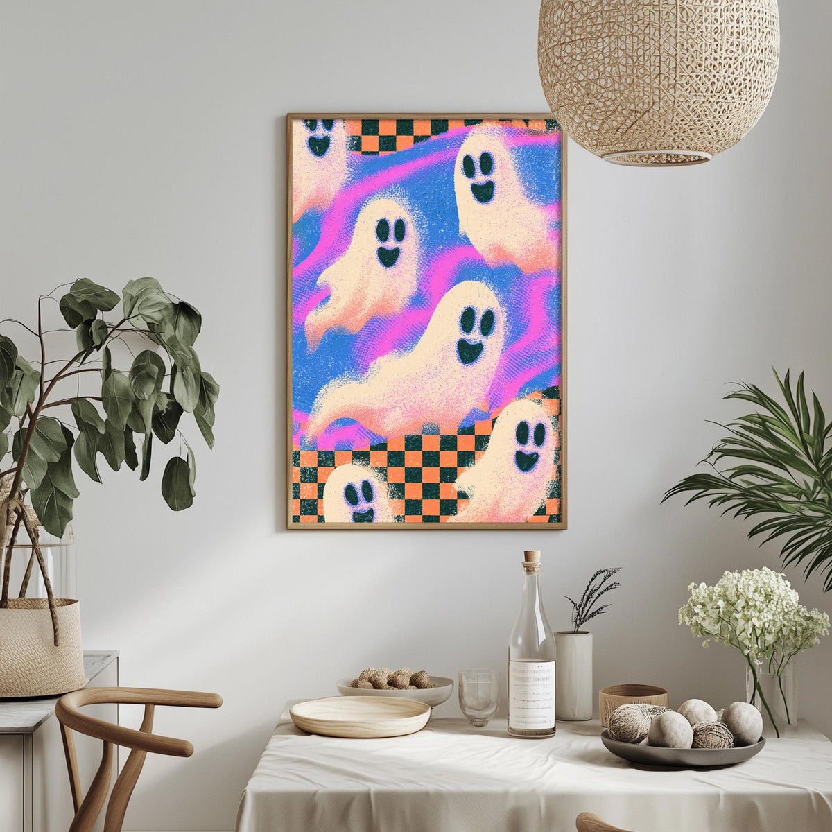 a wall art piece with a vibrant, colorful design of ghostly figures against a checkered background. The art piece is hanging above a dining table, which is set with various items such as a bottle, a bowl, and a vase. The table is surrounded by chairs, creating a cozy and inviting atmosphere. The overall scene appears to be a festive or celebratory setting, possibly for a Halloween or other spooky occasion.