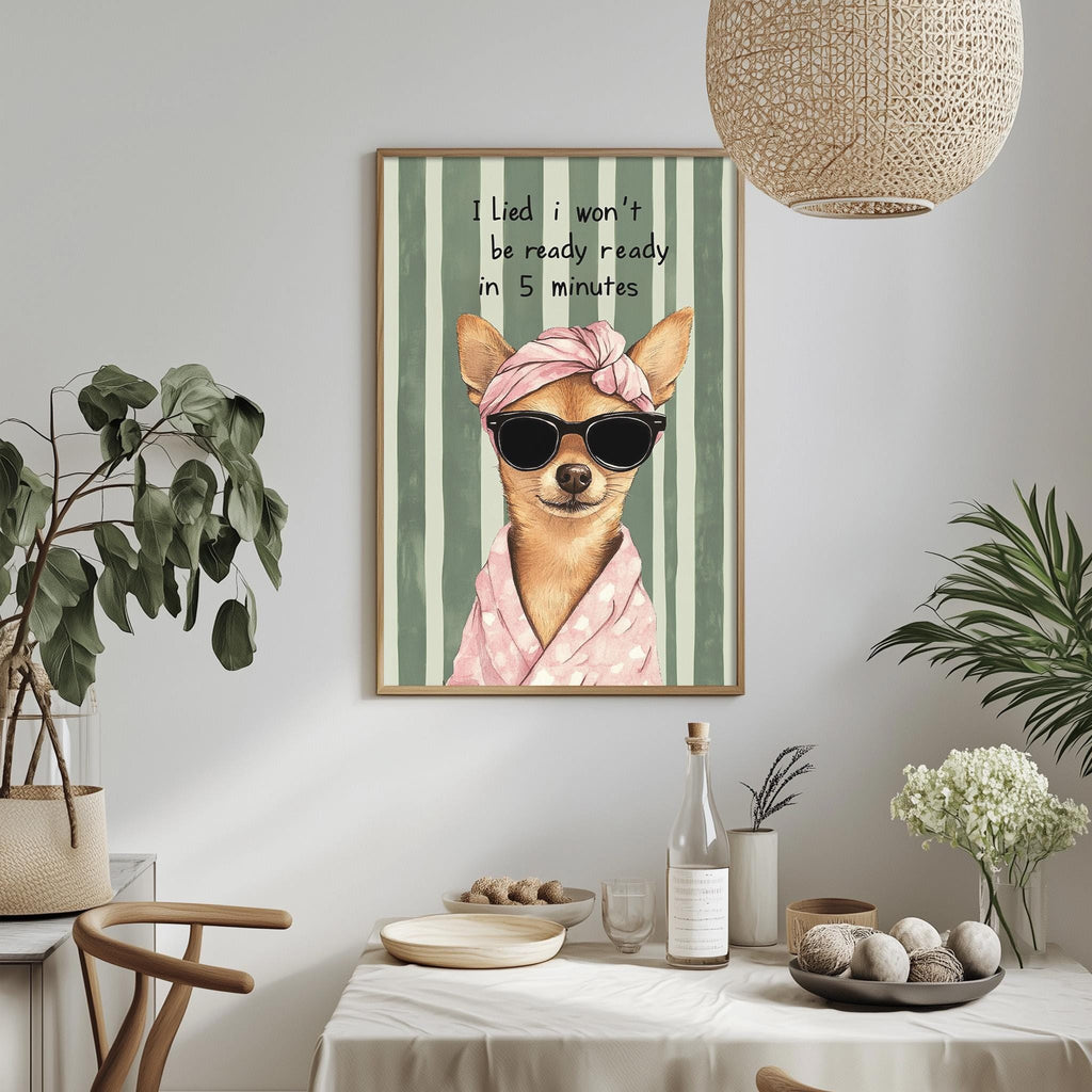 a framed picture of a dog wearing sunglasses and a pink scarf, with the text "I lie, I won't be ready in 5 minutes" written above it. The dog is wearing a pink scarf and sunglasses, and there are potted plants and a dining table in the background.