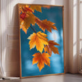 A framed photograph of vibrant autumn leaves in shades of orange and yellow is displayed on a white wall in a room with a window.