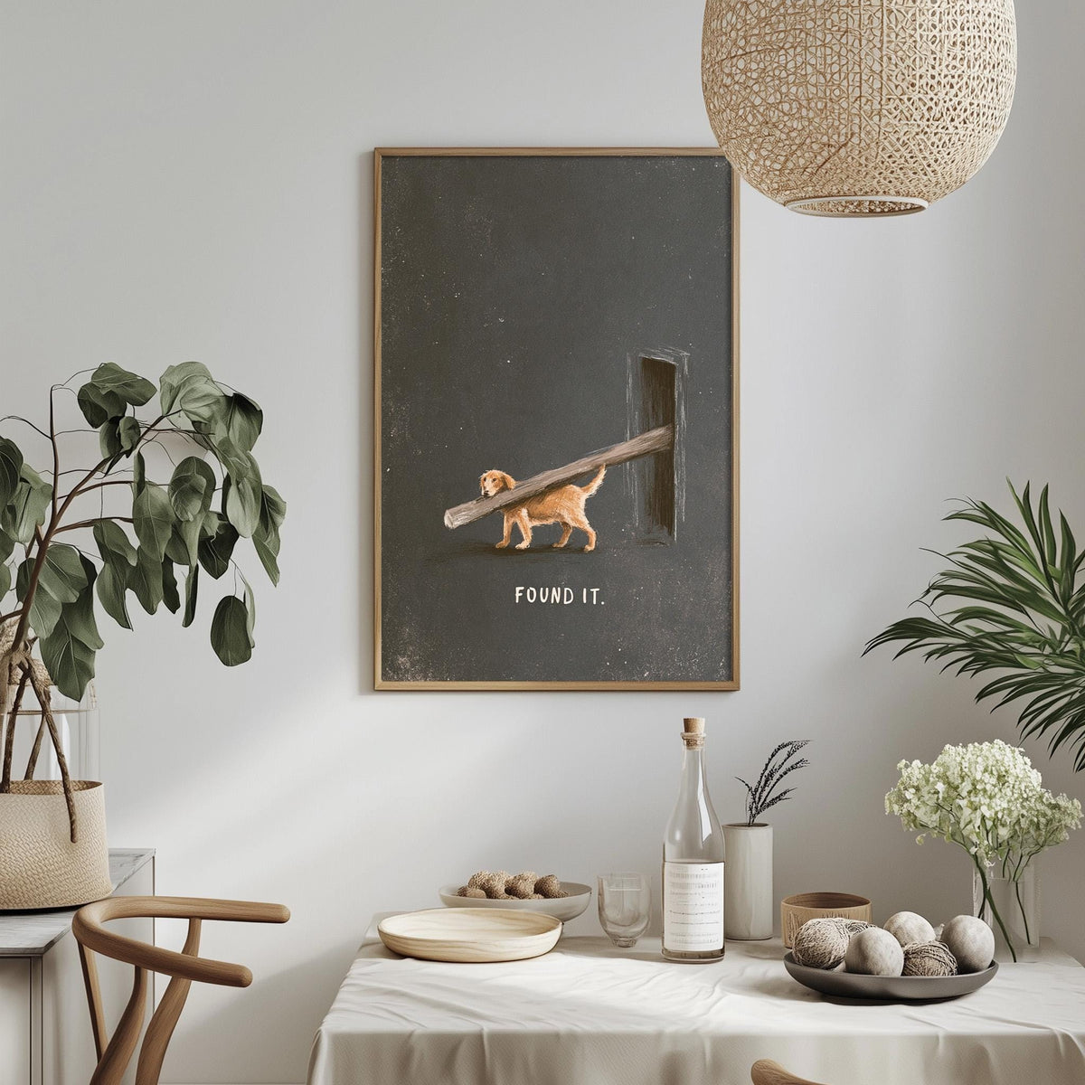 a dining table with a white tablecloth, a bowl of fruit, a bottle, and a vase with flowers. Above the table, there is a framed artwork depicting a dog walking on a branch with the text "FOUND IT" below it.