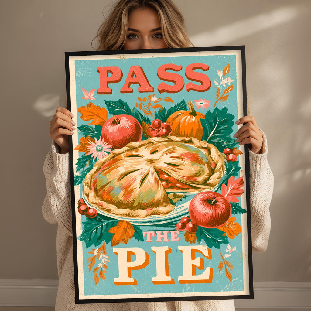 A woman is holding up a framed poster with a colorful illustration of a pie surrounded by autumn leaves and fruits, including apples and pumpkins.