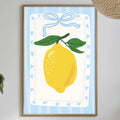 a dining table with a white tablecloth, a bowl of fruit, a bottle, and a vase with flowers. Above the table, there is a framed picture of a lemon with a blue ribbon.