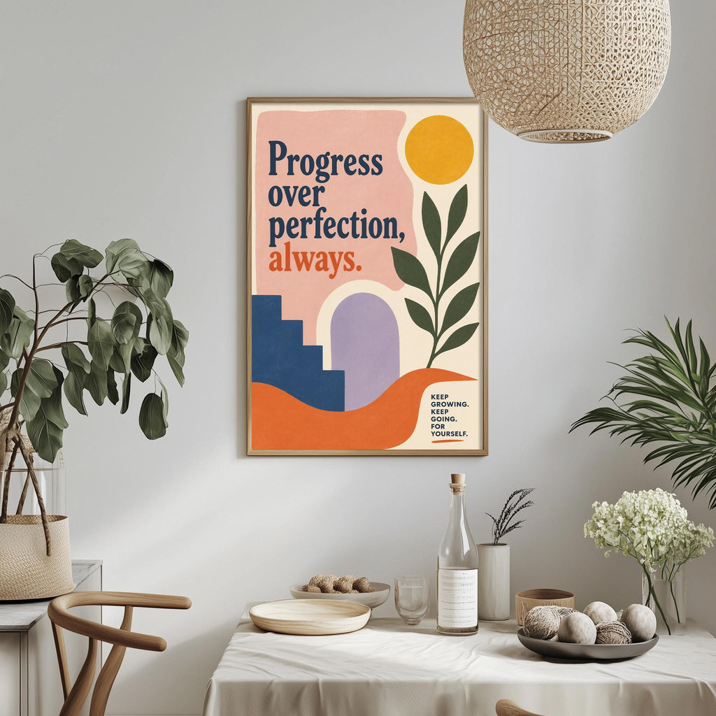a framed poster with the text "Progress over perfection, always" hanging on a wall above a dining table with various items on it, including a bottle, bowls, and a vase.