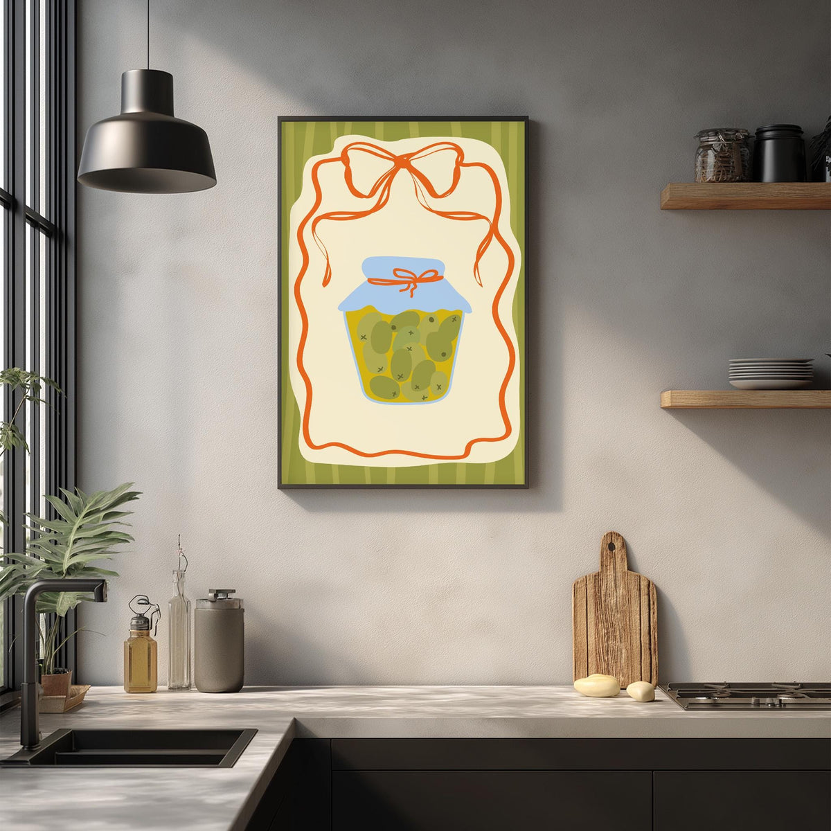 a kitchen counter with various kitchen items, including a framed illustration of a jar of pickles, a wooden cutting board, and a potted plant.