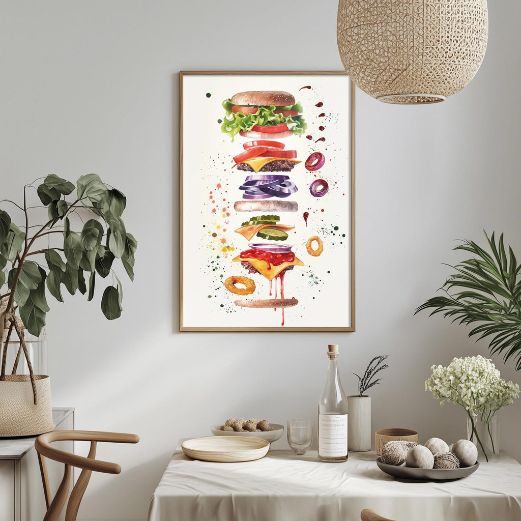 a dining table with a white tablecloth, a bowl of fruit, a bottle, and a vase with flowers. Above the table, there is a framed print of a colorful, watercolor-style illustration of a hamburger.