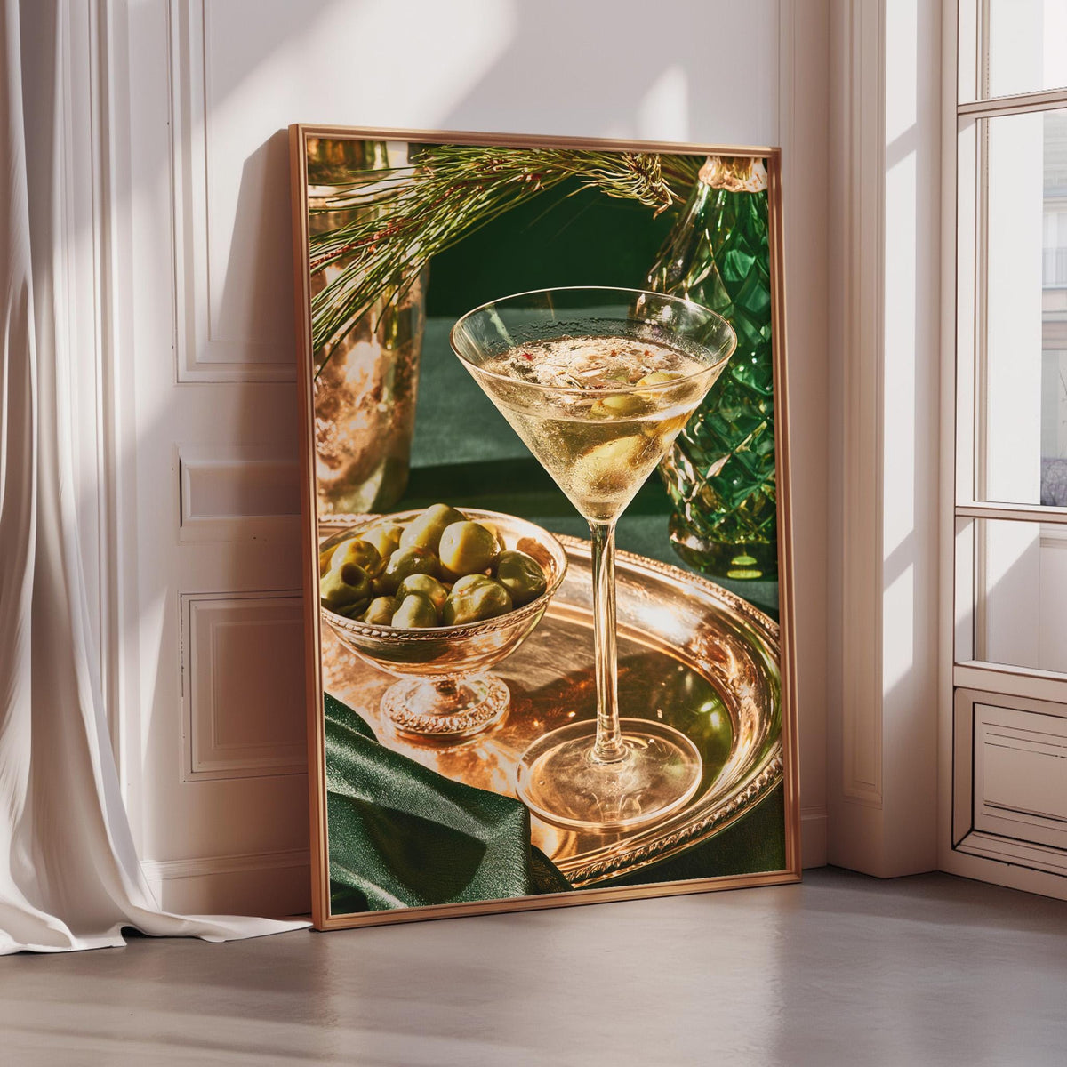 A framed photograph of a martini glass filled with a golden liquid, surrounded by a bowl of green olives and a bottle of olive oil, set against a white wall and a window.