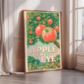 A framed poster with a vibrant illustration of apples hanging from a tree, along with the text "APPLE OF MY EYE" prominently displayed.