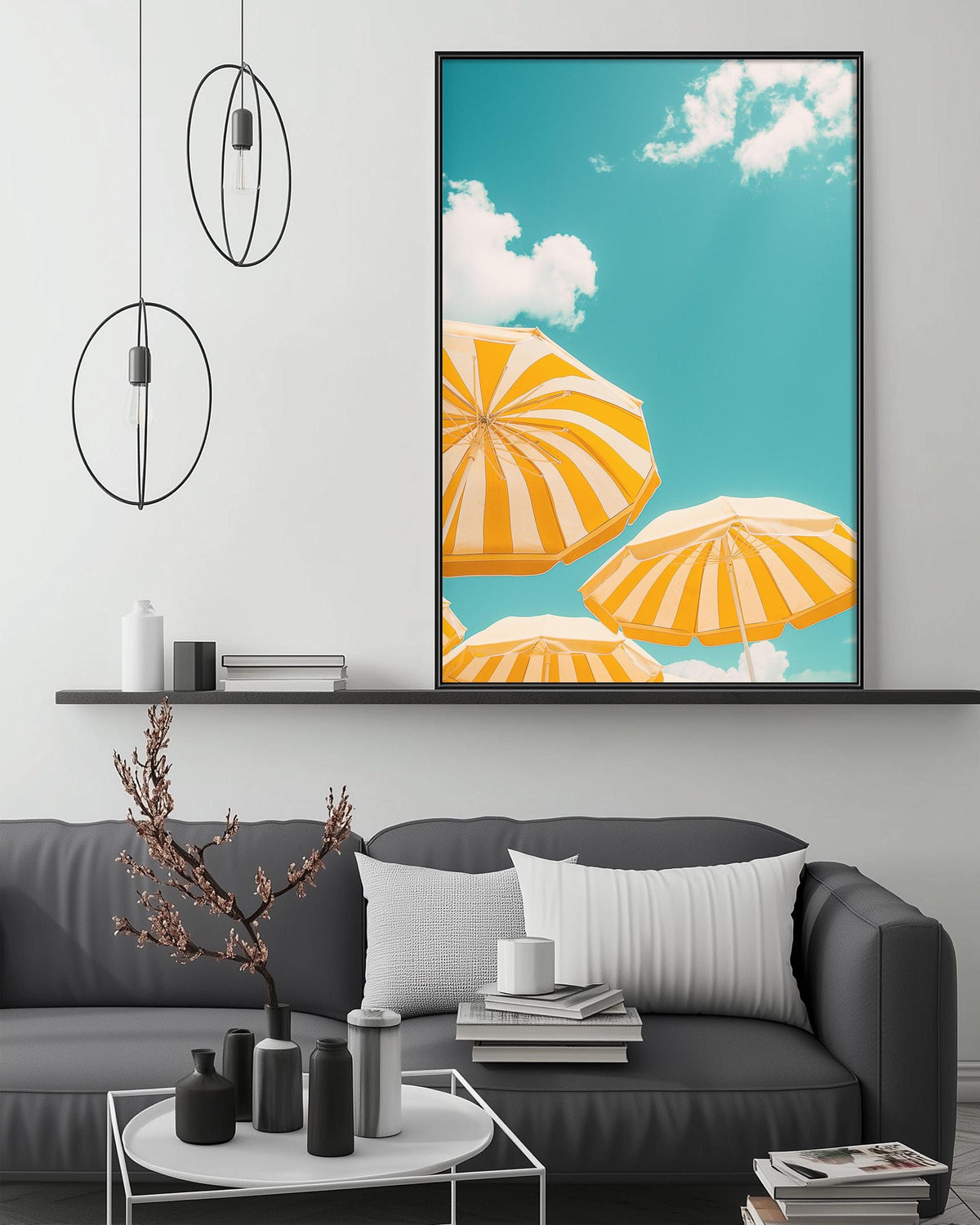 a modern living room with a gray sofa, a coffee table, and a large framed picture of orange and white striped umbrellas against a blue sky with clouds.